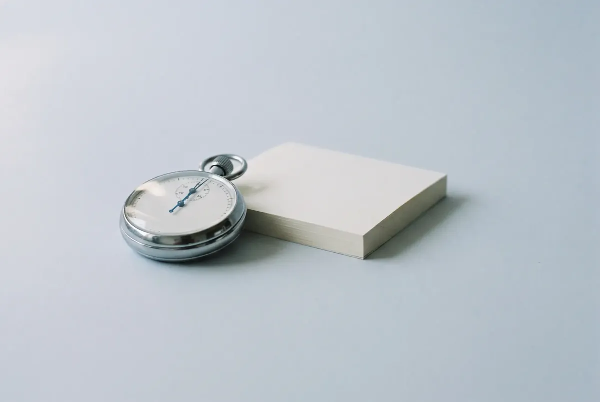 A mechanical stopwatch beside a small stack of blank paper.